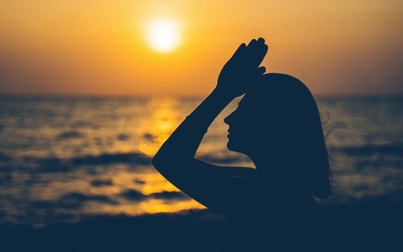 Silhouette of a woman in a powerful yoga pose against a golden sunset.